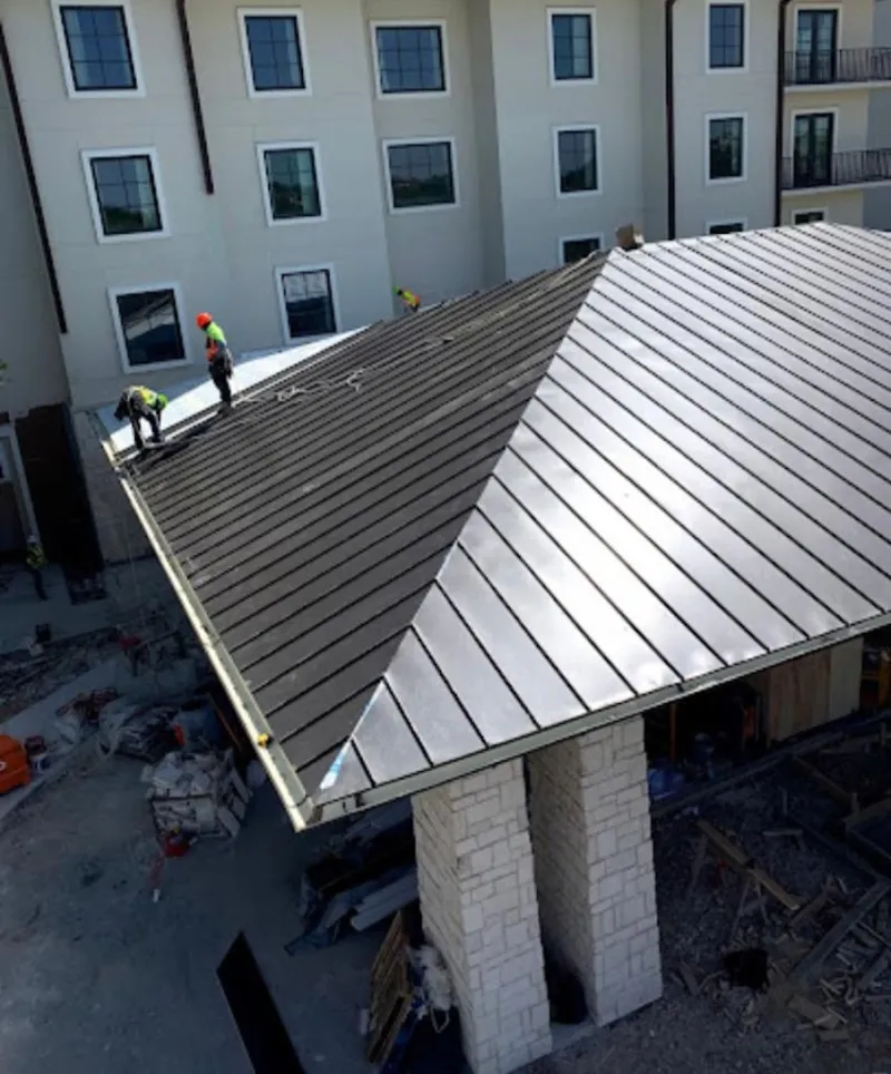 Crew installing standing seam metal roof panels on a commercial project in Lansing